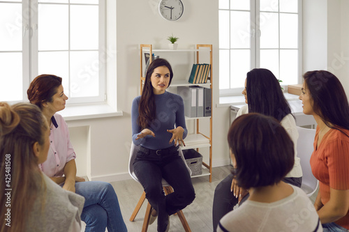 Psychological support. Young woman experienced psychologist talking to other women sitting in a circle during group therapy. Concept of helping women who suffer from abuse and domestic violence.
