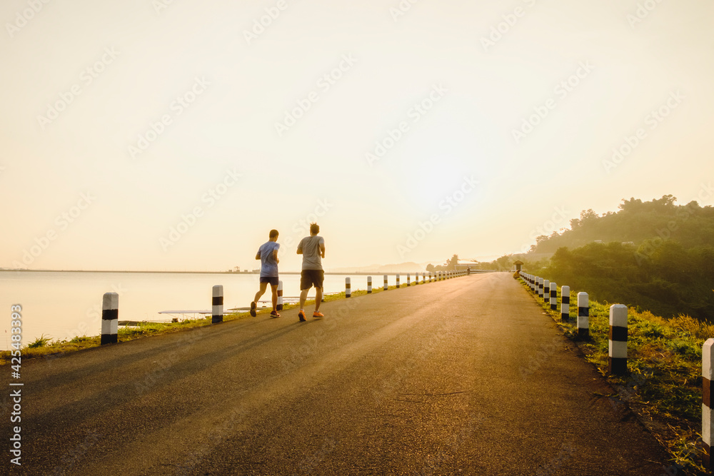Rear View Of Two Man Running On Road Against Sunlight During Sunrise Rear View Of Two Man Running On Road Against Sunlight During Sunrise