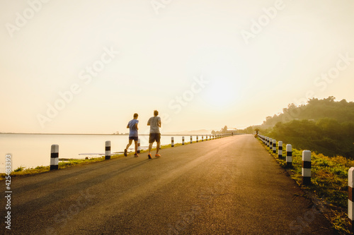 Rear View Of Two Man Running On Road Against Sunlight During Sunrise