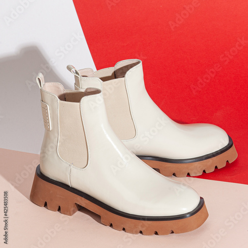 Pair of new white women short boots on medium high heels on beige background studio shot
