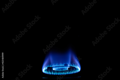Stock photo of gas burner with blue flame on kitchen stove in dark black background, focus on object.