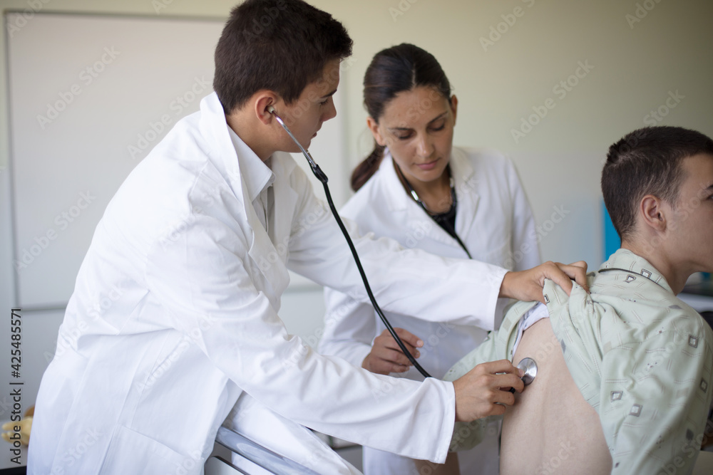 Young student checks a patient's lungs in a hospital room. Young student checks a patient's lungs in a hospital room.