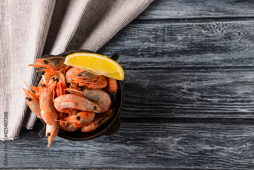 Boiled shrimps served with lemon in a small bowl over rustic wooden background with cloth.