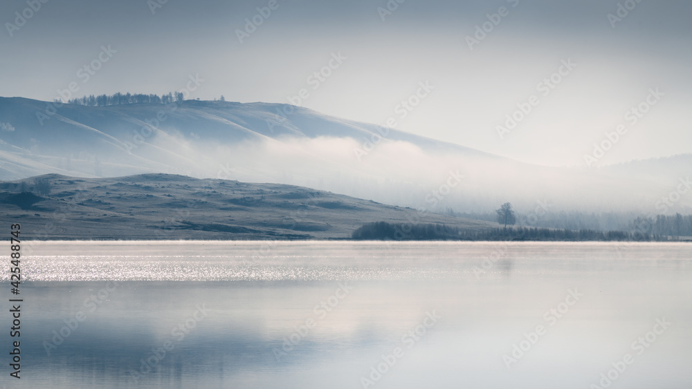 Beautiful lake in misty morning. Mountains reflected in the calm water surface. Autumn landscape. South Ural, Russia.