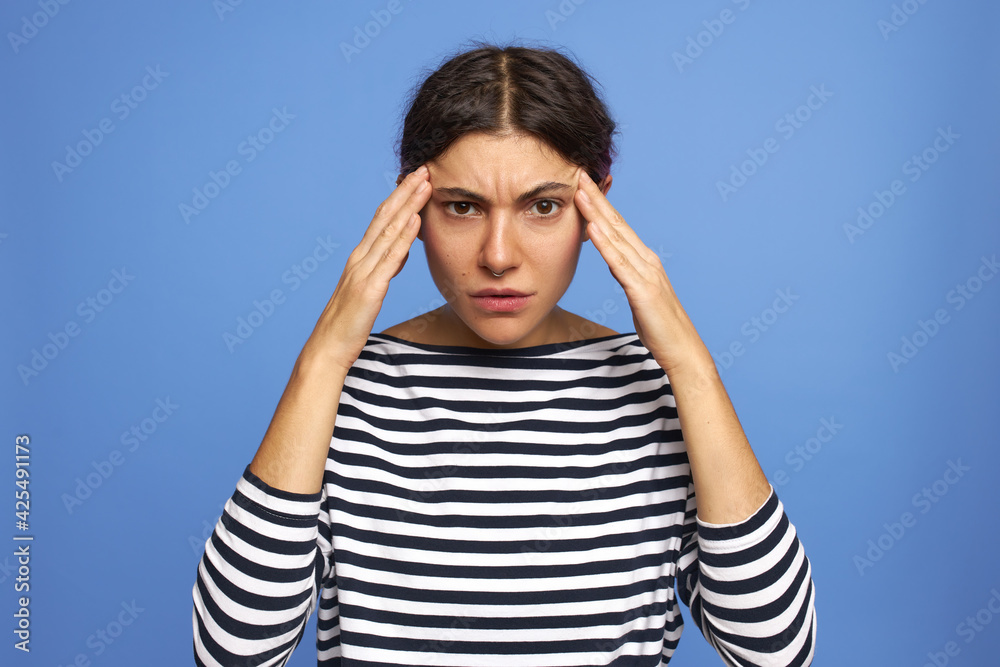 Isolated shot of serious unhappy young female in sailor shirt massaging temples suffering from terrible headache, having high blood pressure. Focused girl trying to remember important information Isolated shot of serious unhappy young female in sailor shirt massaging temples suffering from terrible headache, having high blood pressure. Focused girl trying to remember important information