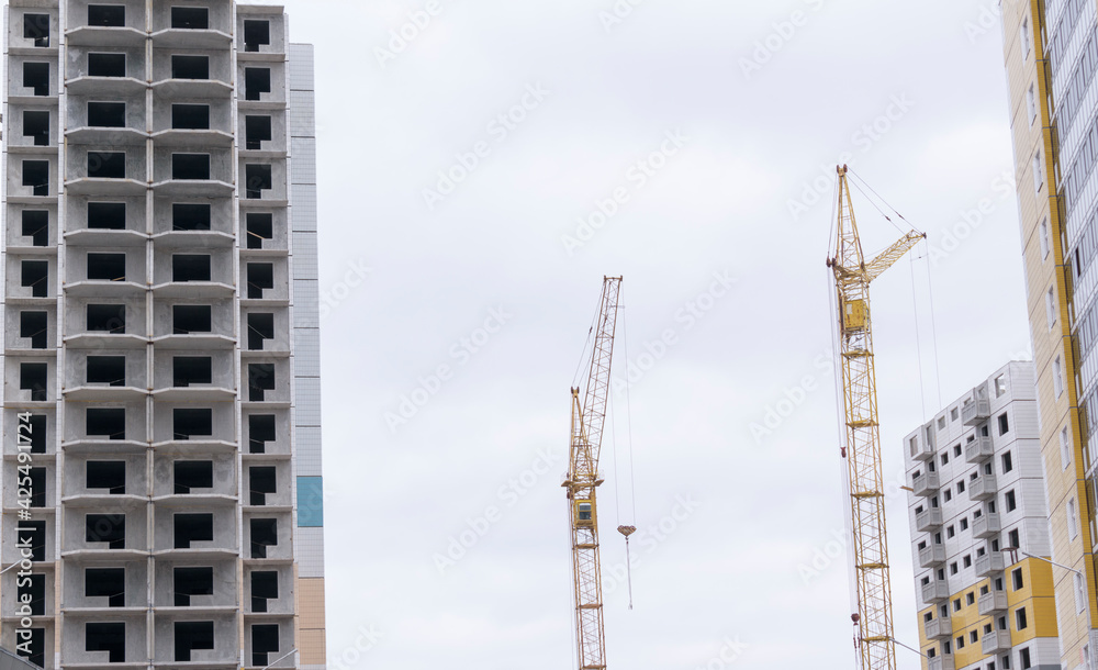 Fototapeta premium Construction of a multi-storey panel house. Tall concrete box. Two high-rise construction cranes. Background - the sky with clouds.