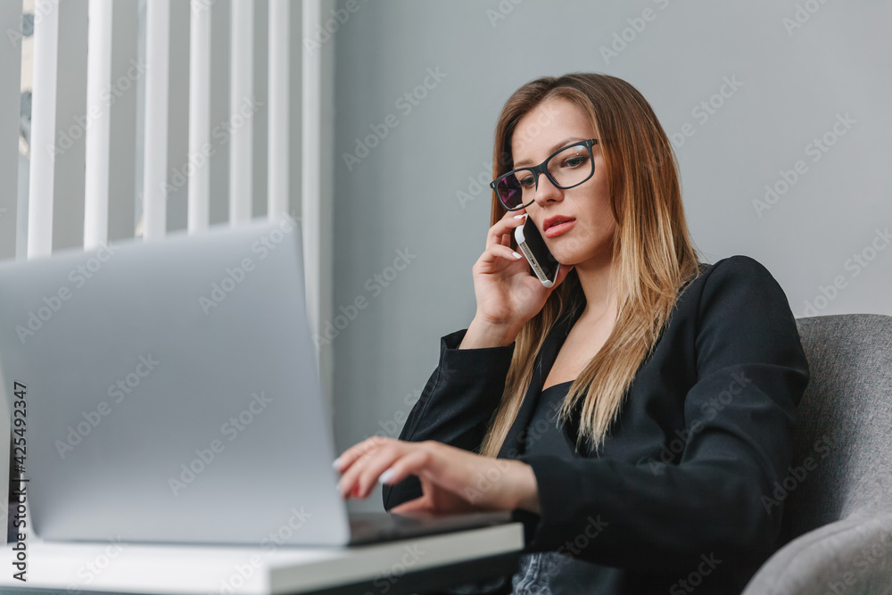 Young business woman talking on cell phone and working on laptop in office Young business woman talking on cell phone and working on laptop in office