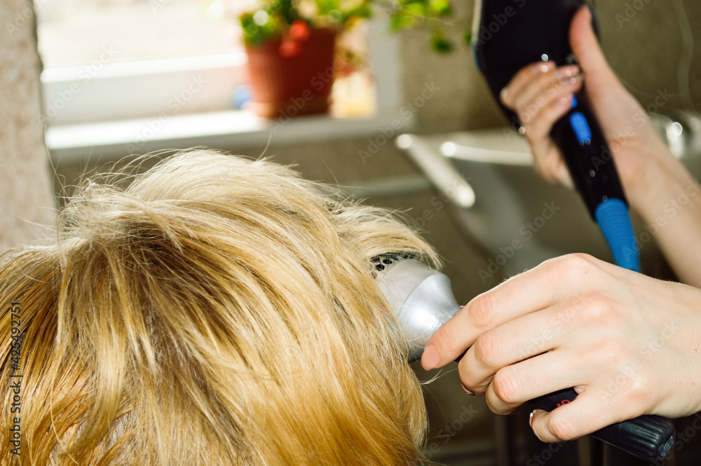 Fototapeta premium close-up - hairdresser dries hair with a hairdryer and styles with a round comb short, blonde hair of a woman after a haircut
