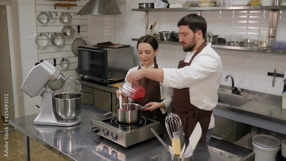 Two chefs cook strawberry jam together in a pot in a professional kitchen. Two chefs cook strawberry jam together in a pot in a professional kitchen.
