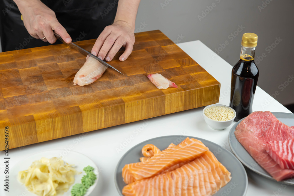 Close up of Chef cook hands chopping salmon fish for traditional Asian cuisine with Japanese knife. Professional Sushi chef cutting seafood for rolls. Close up of Chef cook hands chopping salmon fish for traditional Asian cuisine with Japanese knife. Professional Sushi chef cutting seafood for rolls.