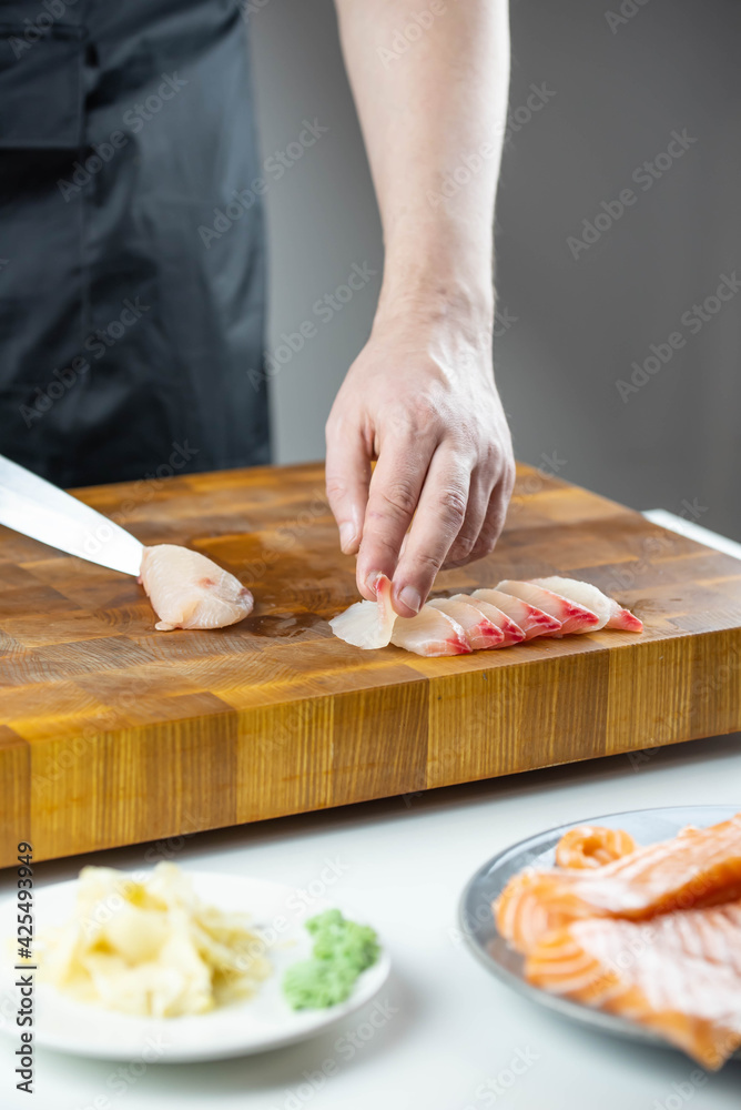 Close up of Chef cook hands chopping salmon fish for traditional Asian cuisine with Japanese knife. Professional Sushi chef cutting seafood for rolls.