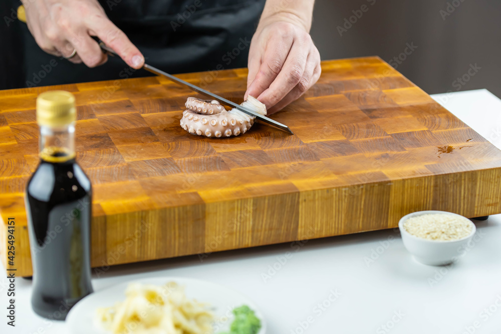 Close up of Chef cook hands chopping octopus for traditional Asian cuisine with Japanese knife. Professional Sushi chef cutting seafood for rolls. Close up of Chef cook hands chopping octopus for traditional Asian cuisine with Japanese knife. Professional Sushi chef cutting seafood for rolls.