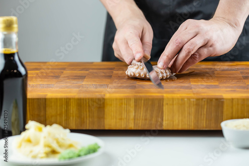 Close up of Chef cook hands chopping octopus for traditional Asian cuisine with Japanese knife. Professional Sushi chef cutting seafood for rolls.