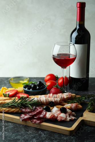 Fototapeta Naklejka Na Ścianę i Meble -  Board with grissini and snacks, and wine on black smokey table