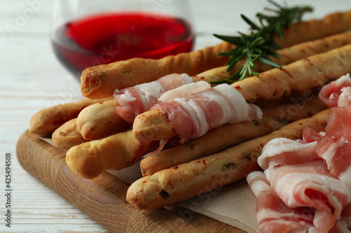Grissini sticks with bacon and wine on white wooden background