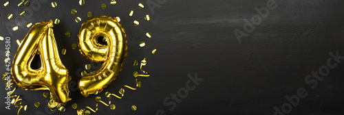 golden foil balloon number forty nine. Birthday or anniversary card with the inscription 49. Black concrete background. Anniversary celebration. Banner. © mtrlin
