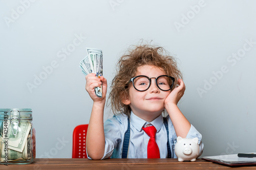 Happy successful business baby girl holding money in hand. Bunch of money. Pupil in glasses. Little businessman. humorous picture.