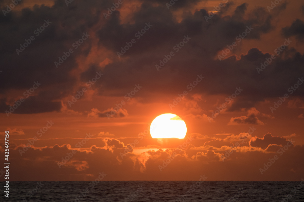 Big sun setting in Ocean painting orange the sky and the clouds