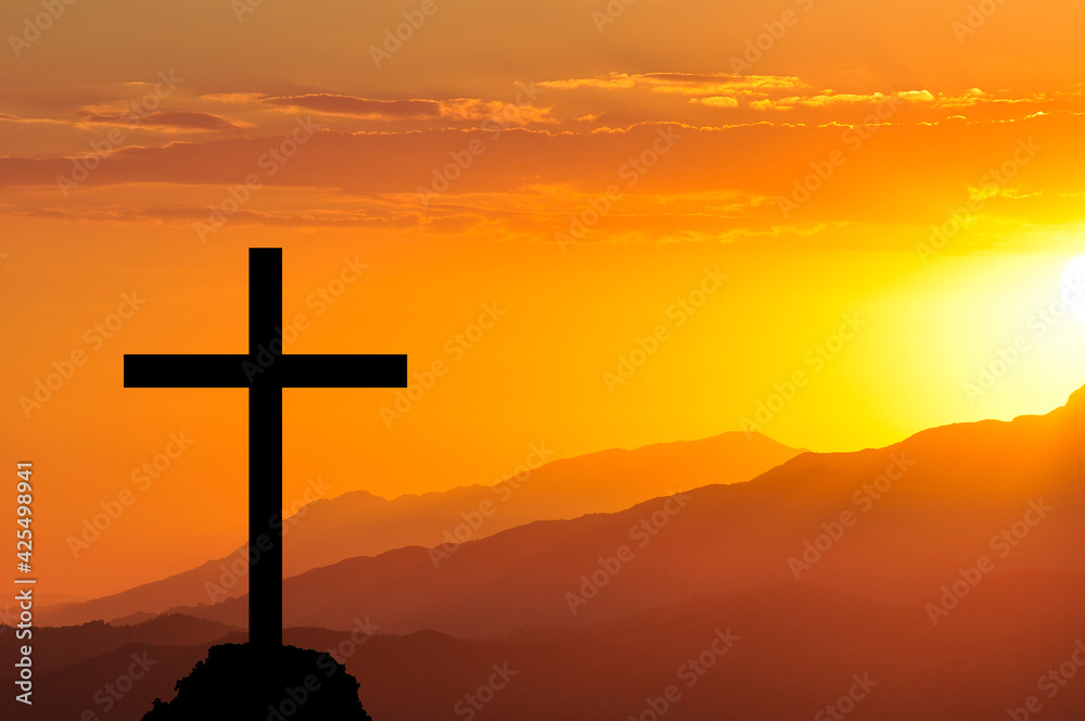 Christian cross outline on the background of the setting yellow sun in the mountains