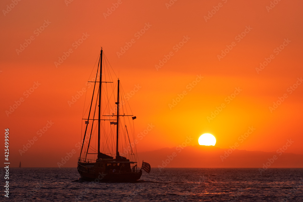 Silhouette of sailing boat with sails down against sun at sunset, sun glare on sea waters. Romantic seascape. Holiday lifestyle landscape 