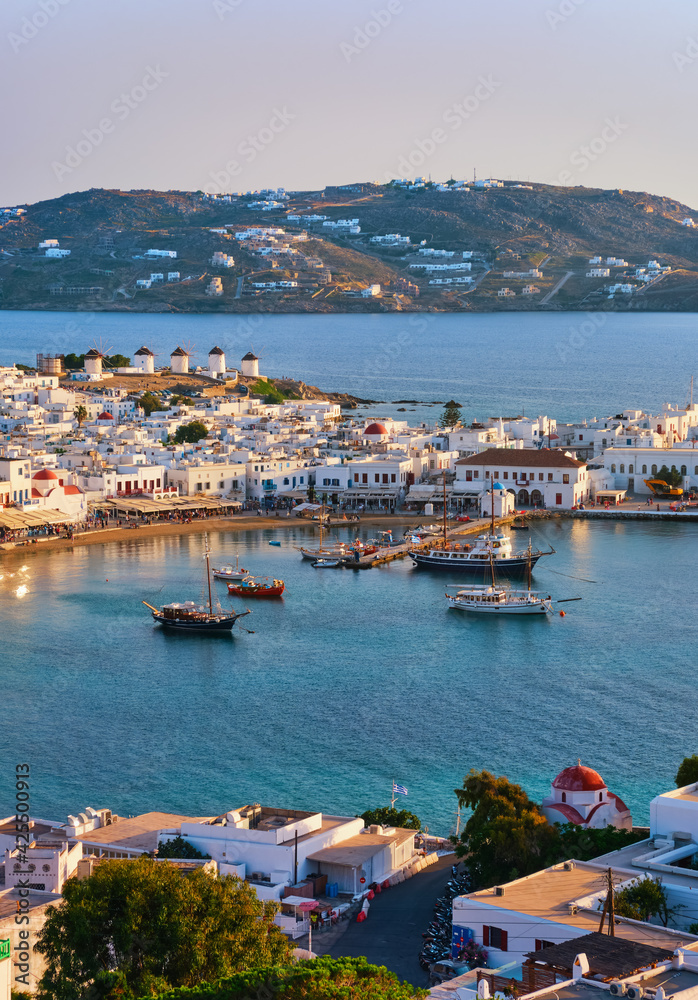Beautiful sunset view of Mykonos, Cyclades, Greece, its port, windmills. Cruises, ship, whitewashed houses. Vacation, leisure, Mediterranean lifestyle