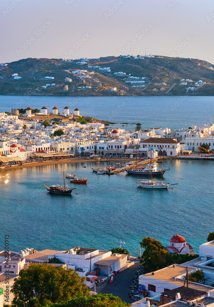 Fototapeta premium Beautiful sunset view of Mykonos, Cyclades, Greece, its port, windmills. Cruises, ship, whitewashed houses. Vacation, leisure, Mediterranean lifestyle