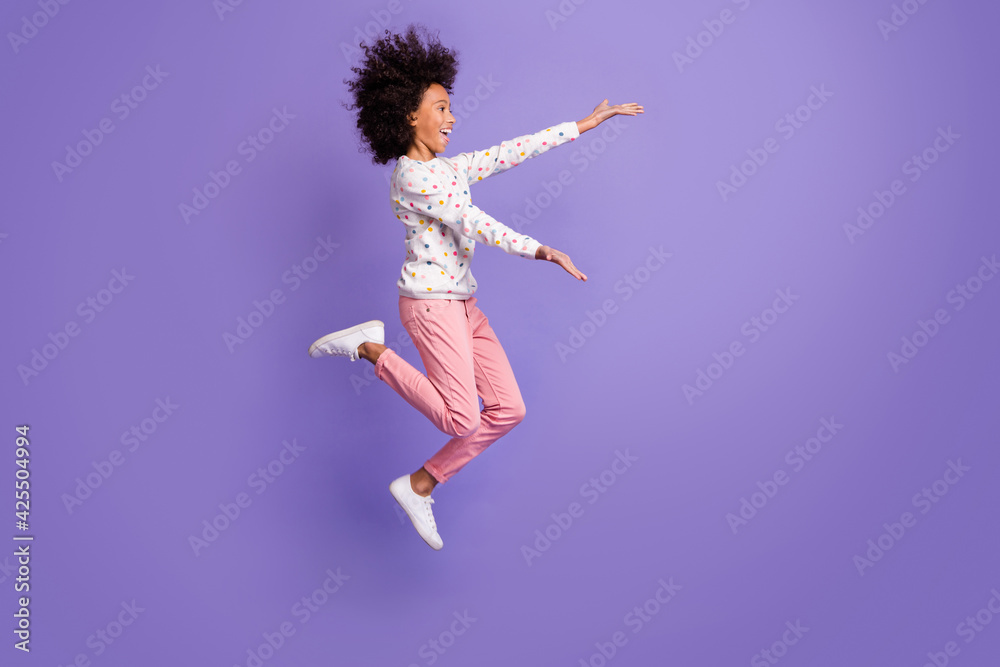 Full size profile side photo of afro american little girl jump open hands copyspace isolated on violet color background Full size profile side photo of afro american little girl jump open hands copyspace isolated on violet color background