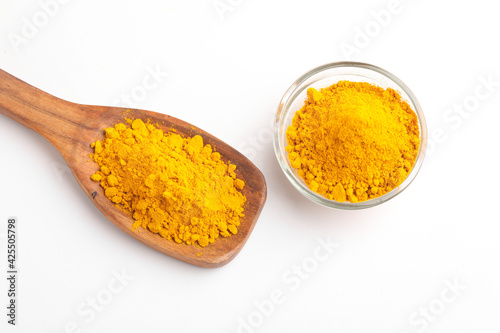 Turmeric powder in wooden spoon and glass bowl on white background.