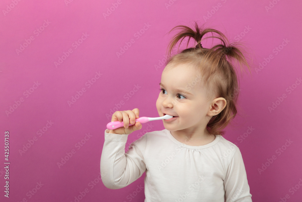 Cute baby girl brushing teeth on pink background. Foto with copy space for text Cute baby girl brushing teeth on pink background. Foto with copy space for text