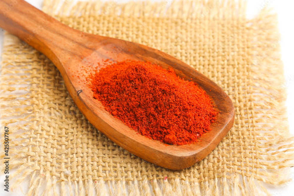close view of red chilli powder in wooden spoon on white background.