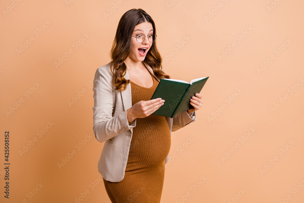 Photo of sweet impressed lady waiting baby dressed brown dress tummy reading book isolated beige color background Photo of sweet impressed lady waiting baby dressed brown dress tummy reading book isolated beige color background
