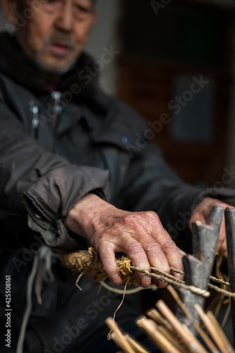 An old man is making straw sandals in his house.