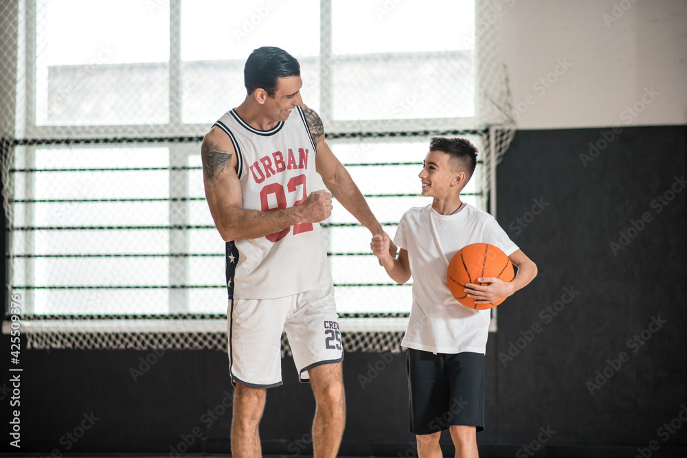 Coach in white sportswear teaching the boy playing basketball Coach in white sportswear teaching the boy playing basketball