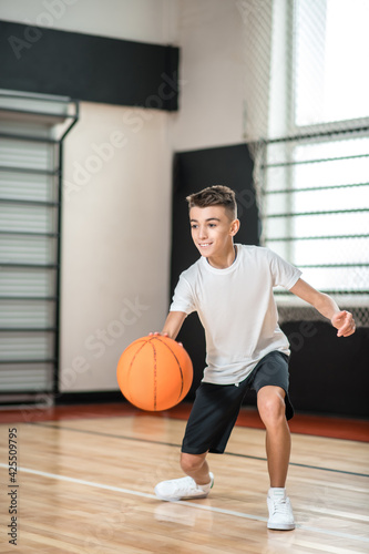 Teen in white tshirt playing basketball in the gym and looking involved © zinkevych