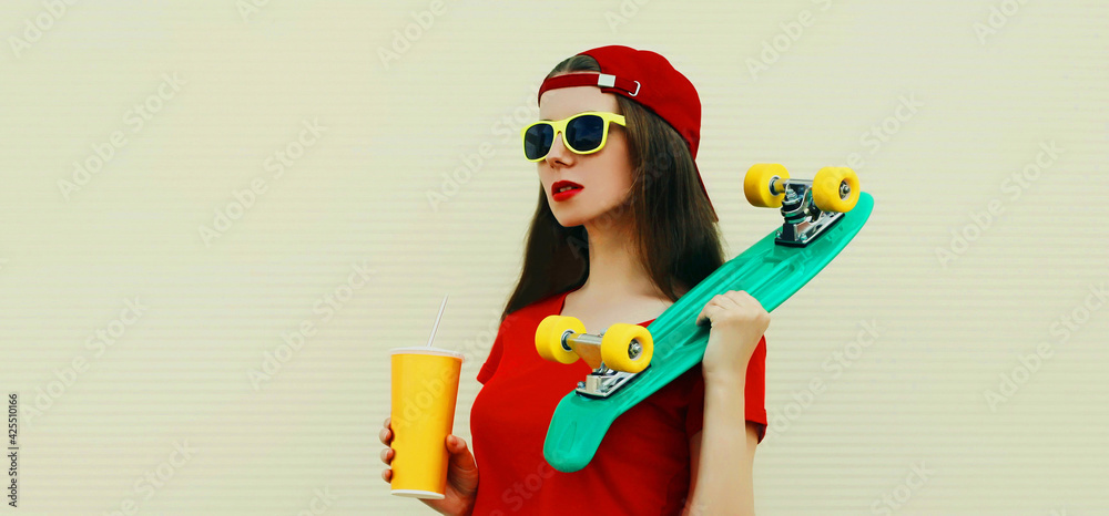 Summer portrait of young woman with cup of juice and green skateboard wearing a red baseball cap Summer portrait of young woman with cup of juice and green skateboard wearing a red baseball cap