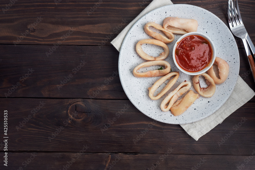 Fried squid rings with tomato sauce and lemon. Dark wooden background copy space. Top view. Fried squid rings with tomato sauce and lemon. Dark wooden background copy space. Top view.