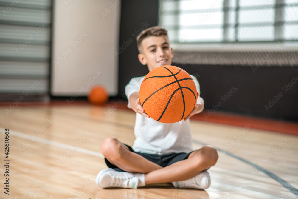 A dark-haired boy sitting on the floor and holding a ball in hands A dark-haired boy sitting on the floor and holding a ball in hands