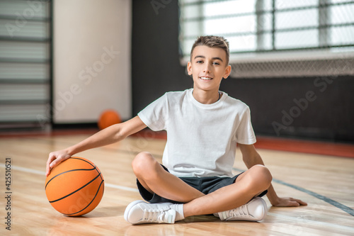 A dark-haired boy sitting on the floor and holding a ball in hands © zinkevych