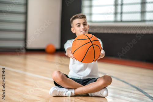 A dark-haired boy sitting on the floor and holding a ball in hands