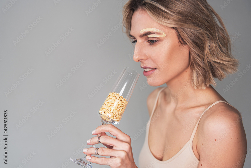 Portrait of a girl of European appearance on a light background with a glass filled with wax
