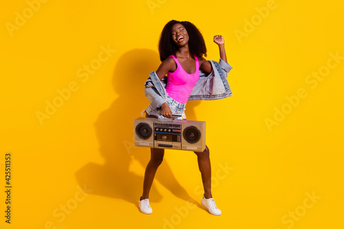 Full body photo of young attractive black girl happy positive smile listen music boombox dance isolated over yellow color background