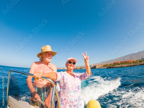 Beautiful and cute couple of seniors or old people in the middle of the sea driving and discovering new places with small boat. Mature woman holding a phone and taking a selfie with hew husband
