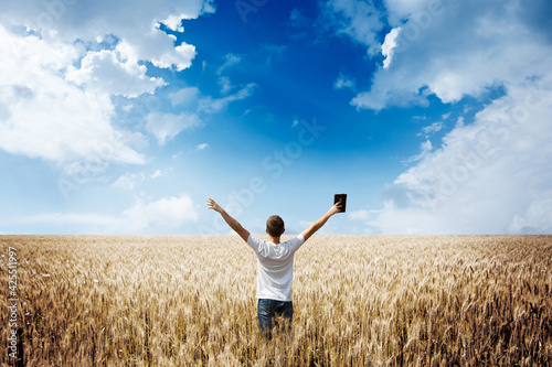Man holding up Bible in a wheat field