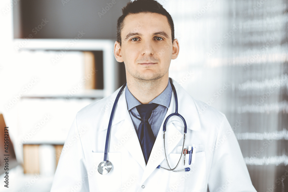 Male doctor standing straight in clinic near his working place. Perfect medical service in hospital. Medicine and healthcare concept Male doctor standing straight in clinic near his working place. Perfect medical service in hospital. Medicine and healthcare concept