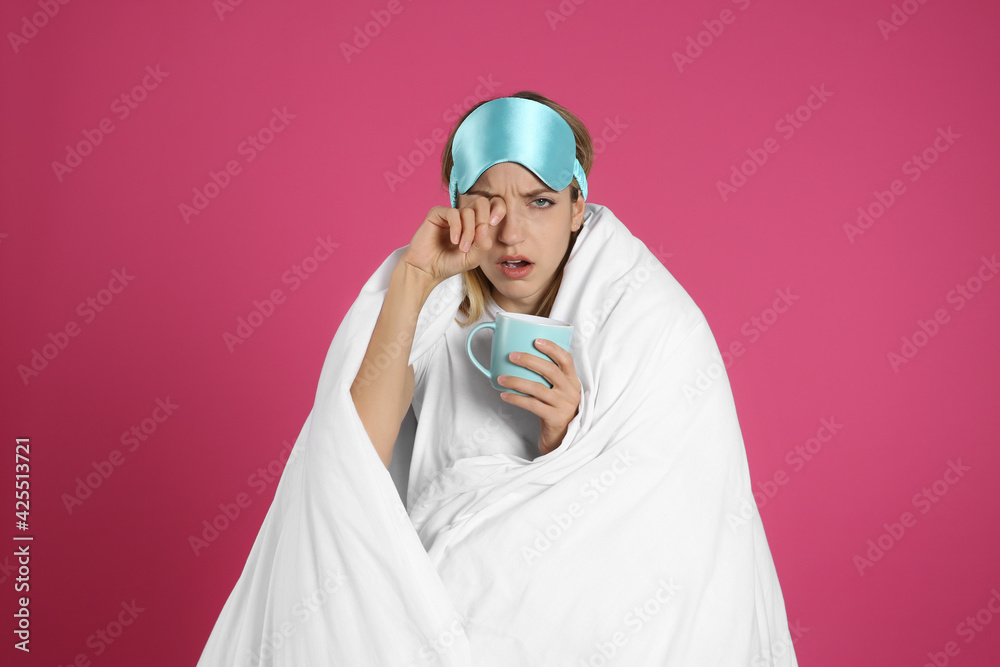 Young woman in sleeping mask wrapped with blanket holding cup on pink background Young woman in sleeping mask wrapped with blanket holding cup on pink background
