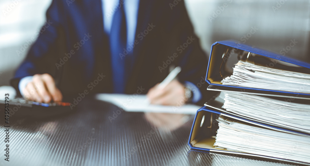 Binders with papers are waiting to be processed by man accountant in blue blazer staying at home during covid pandemic. Taxes and audit concept. Internal Revenue Service inspector checking financial Binders with papers are waiting to be processed by man accountant in blue blazer staying at home during covid pandemic. Taxes and audit concept. Internal Revenue Service inspector checking financial