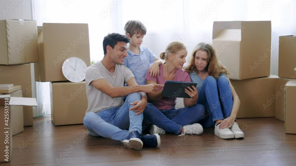 Cheerful and beautiful caucasian mother holding digital tablet and shopping for furniture for new home with handsome husband and children with cardboard boxes around Cheerful and beautiful caucasian mother holding digital tablet and shopping for furniture for new home with handsome husband and children with cardboard boxes around
