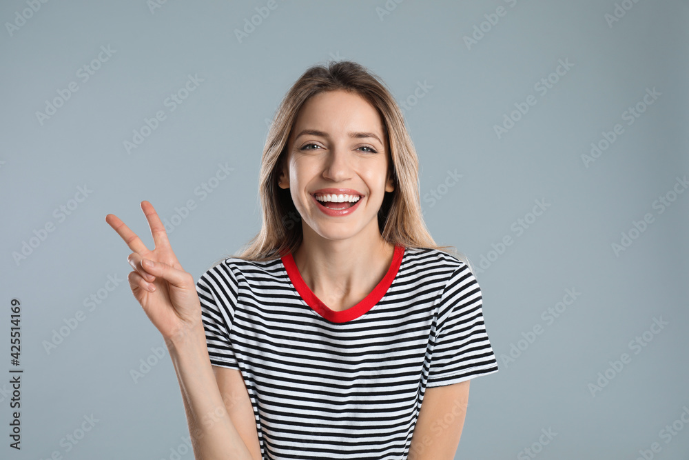 Woman showing number two with her hand on light grey background