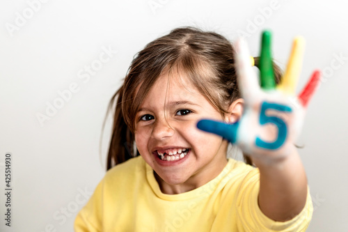 Happy toothless little girl with the five number painted on the hand laughing and having fun - Little girl who is painting her hands with numbers - The number five and childhood concept
