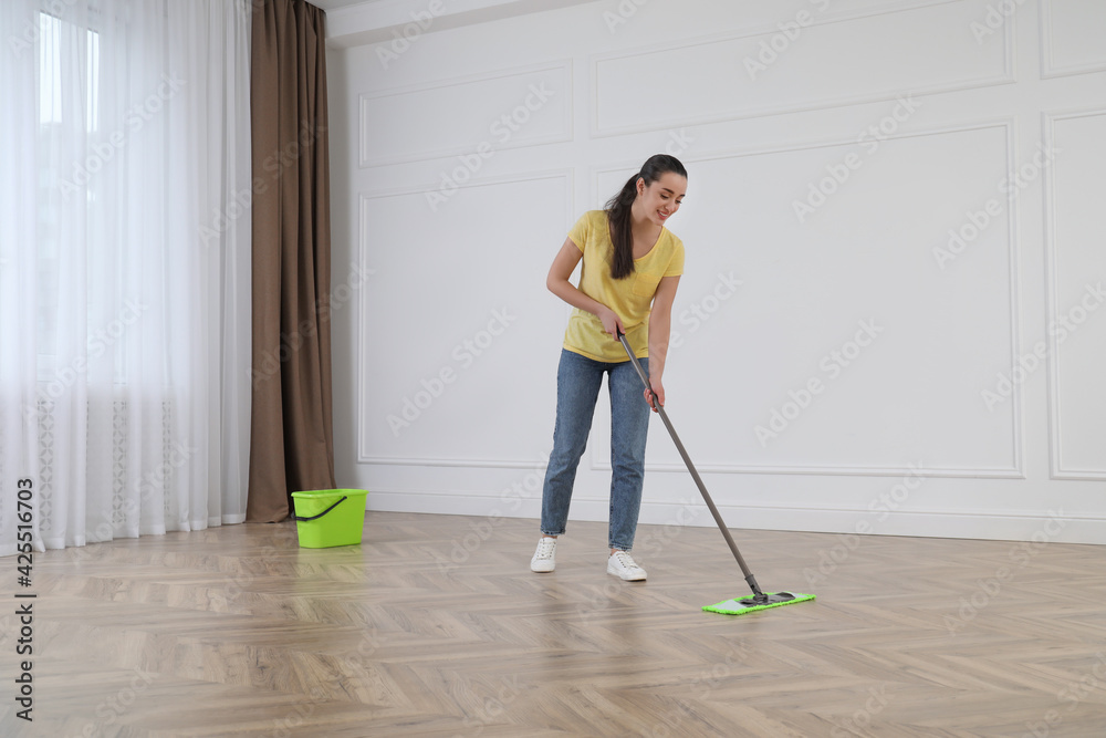 Young woman cleaning floor with mop in empty room Young woman cleaning floor with mop in empty room